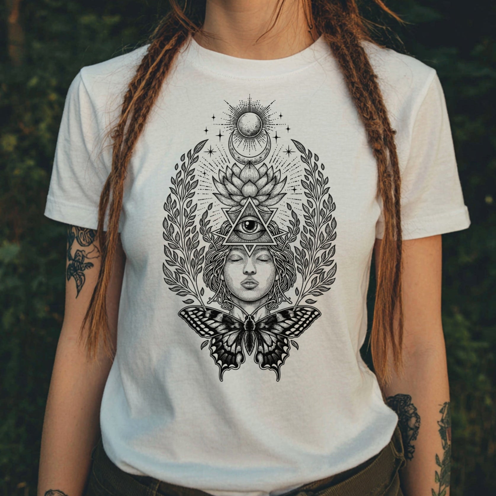 Person wearing a white t-shirt with black intricate design in a forest setting